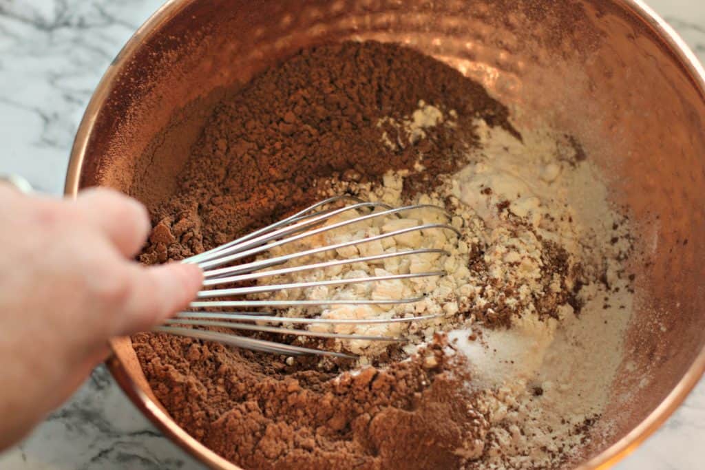 Mixing ingredients for Sour Cream Chocolate Cake in a copper bowl with a whisk