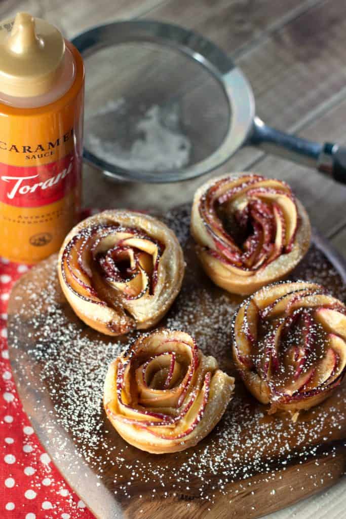 Caramel Apple Rose Tarts dusted with powdered sugar on a rustic wood platter