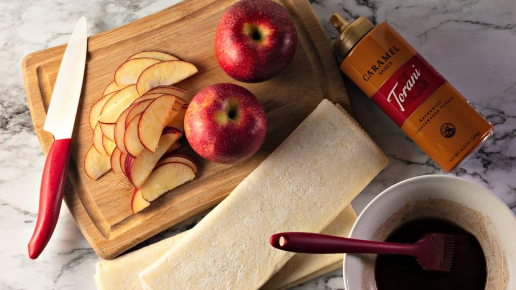 Slicing tart red apples on a bamboo cutting board on a marble counter for making Caramel Apple Rose Tarts