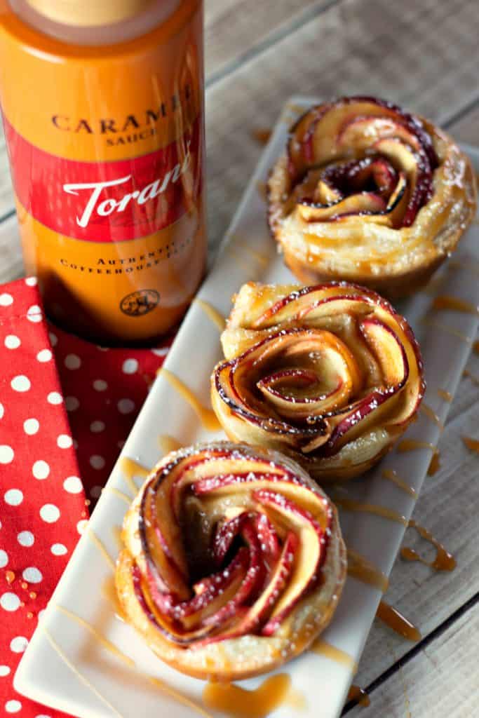 Caramel Apple Rose Tarts on a white rectangle place drizzled with Troani Caramel Sauce with a red and white polka dot napkin