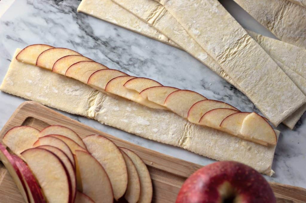 Placing sliced apples onto strips of puff pastry for making Caramel Apple Rose Tarts