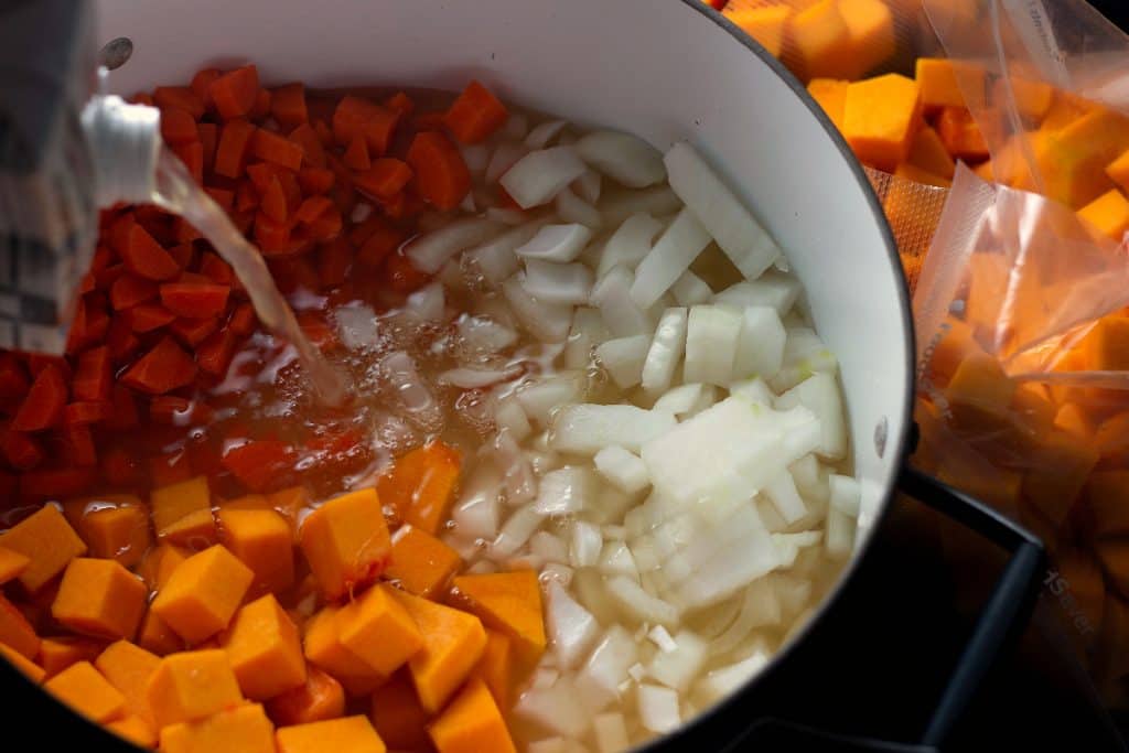 Adding chicken stock to the pot of Savory Butternut Squash Soup