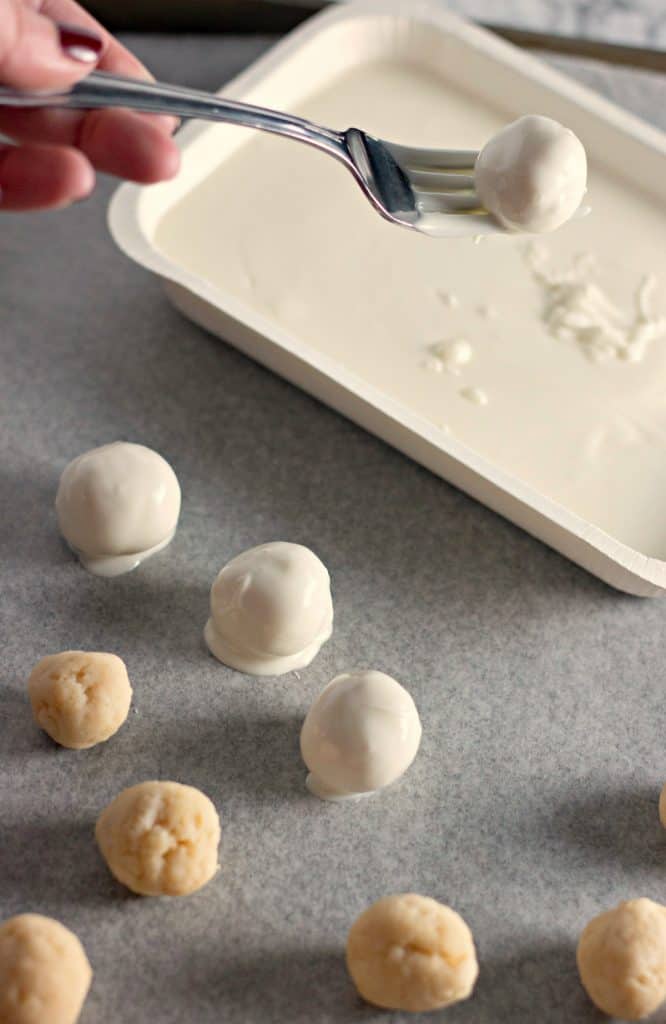 Dipping Christmas Sugar Cookie Truffles into melted vanilla candy coating