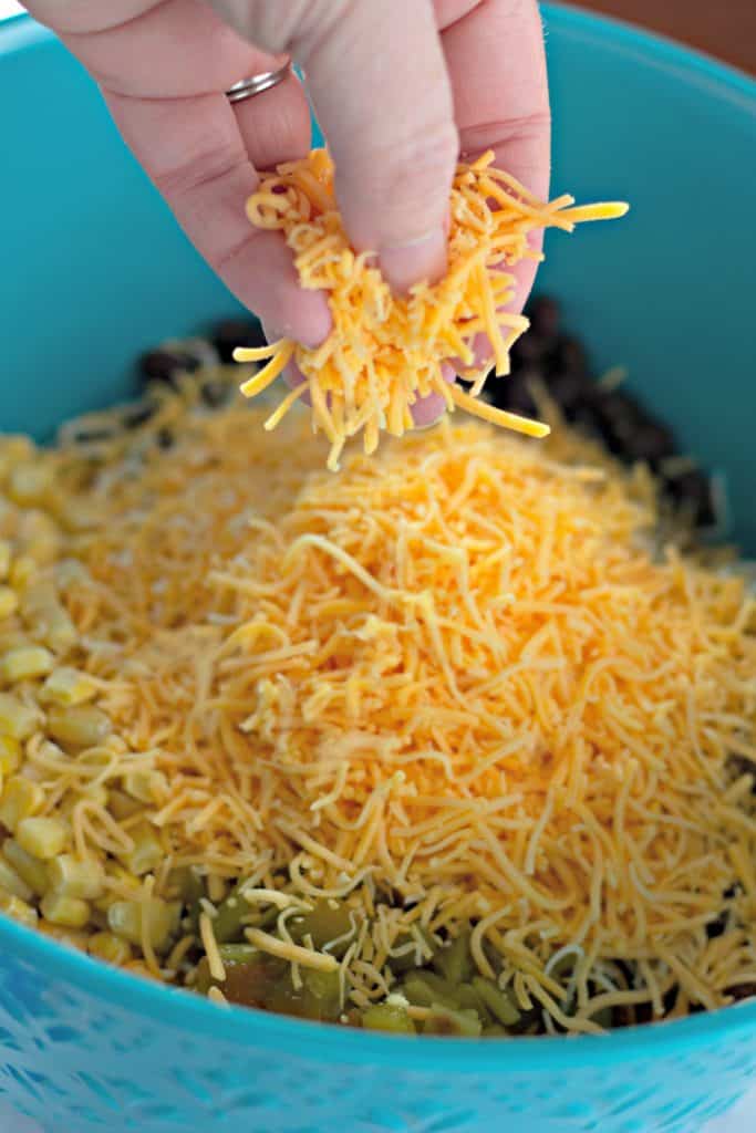Adding shredded cheddar cheese to a teal blue mixing bowl