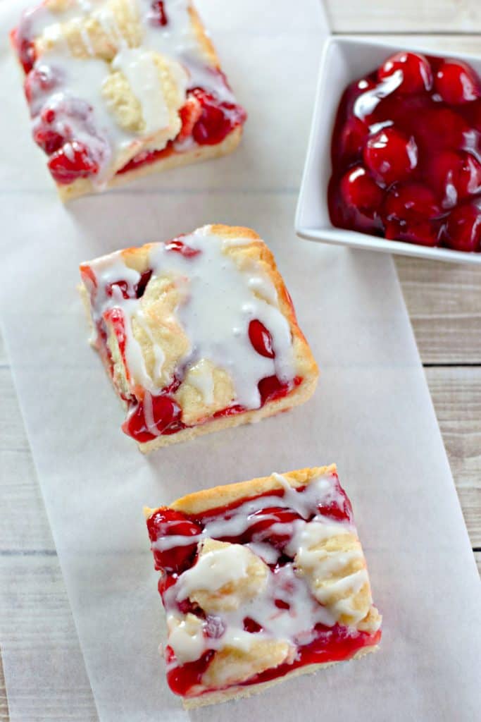 Cherry Pie Bars on parchment paper with a small dish of cherries