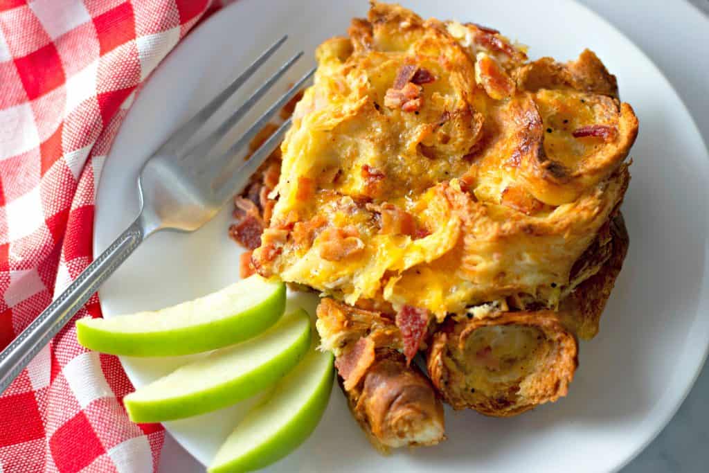 Overnight Bacon Croissant Breakfast Casserole on a white plate with a fork and green apples