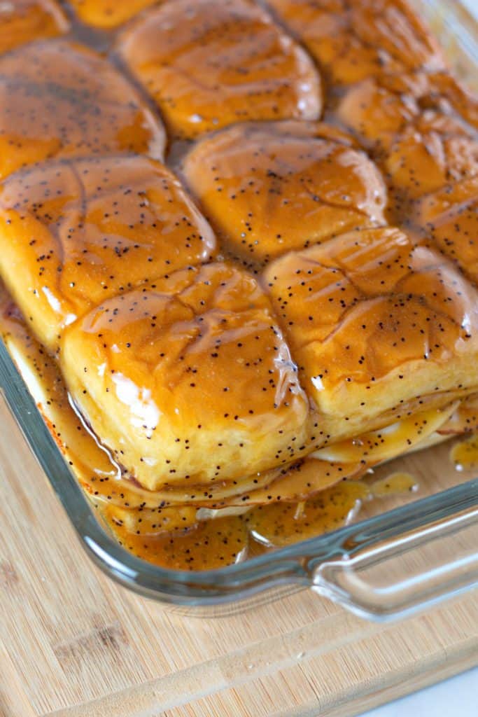 pouring the poppy seed glaze over the sandwiches in the dish.